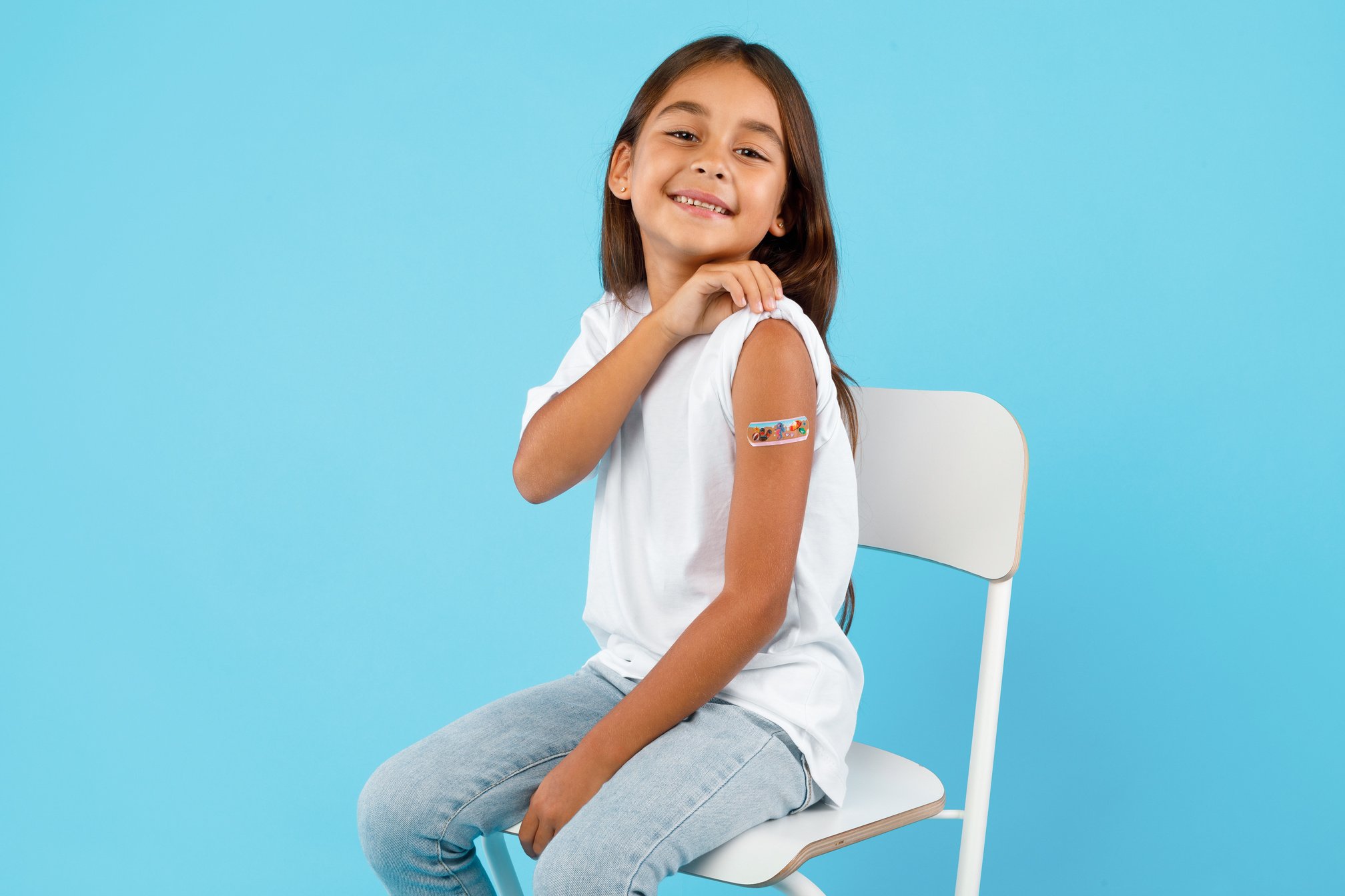 Happy Vaccinated Kid Girl Showing Arm after Vaccination, Blue Background